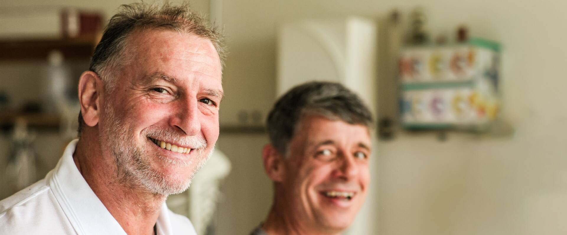 Physiotherapeut lacht, etwas nach hinten versetzt ein lachender Patient