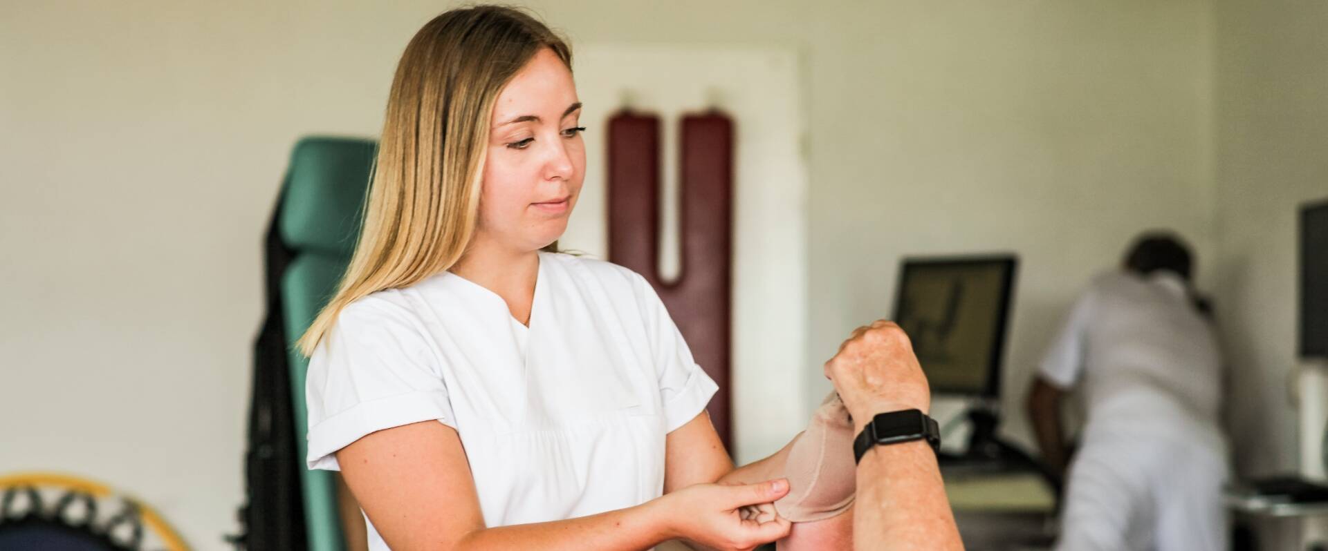 Physiotherapeutin hilft Patienten beim Überziehen einer Bandage 